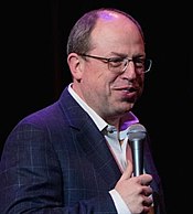 man in dark suit smiling with microphone