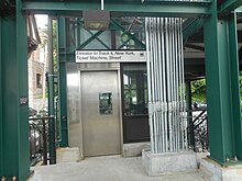 Green steel girders framing a steel sliding door with a window. Above it a sign reads "Elevator to Track 4, New York City, Ticket Machine, Street".