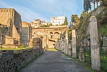 allée avec un bâtiment à gauche, des colonnes à droite et au fond, étage en arcades