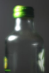 A glass bottle with a green bottlecap; the lens has applied a heavy soft focus effect, resulting in halation around highlights and a hazy, dreamy texture.