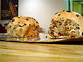 Two loaves of bread with sultanas and raisins, served on a tray. The tray is placed on a wooden table. One of the loaf is slightly cut.