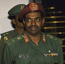 Photographie en couleurs d'un homme noir en uniforme militaire vert paré de décorations, portant un béret rouge. Seul le haut de son corps est visible