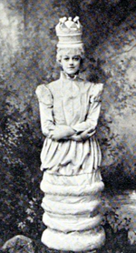 young white woman in white costume, made to look like a queen chess piece, with white hair and white crown