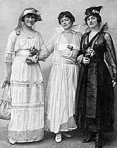 three young white women, standing, arms linked, wearing lavish costumes of mid-1910s