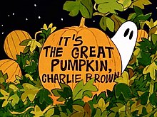 The words "It's the Great Pumpkin, Charlie Brown" written on a pumpkin with leaves around it and a ghost with black eyes behind it. Other pumpkins and the night sky can be seen in the background.