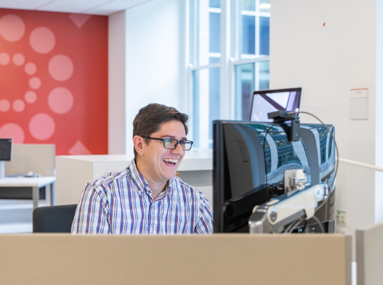 Federal worker showing excitement about information being displayed on their monitor with a red accent wall in the background.