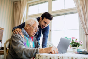 Caretaker and senior man using laptop in nursing home