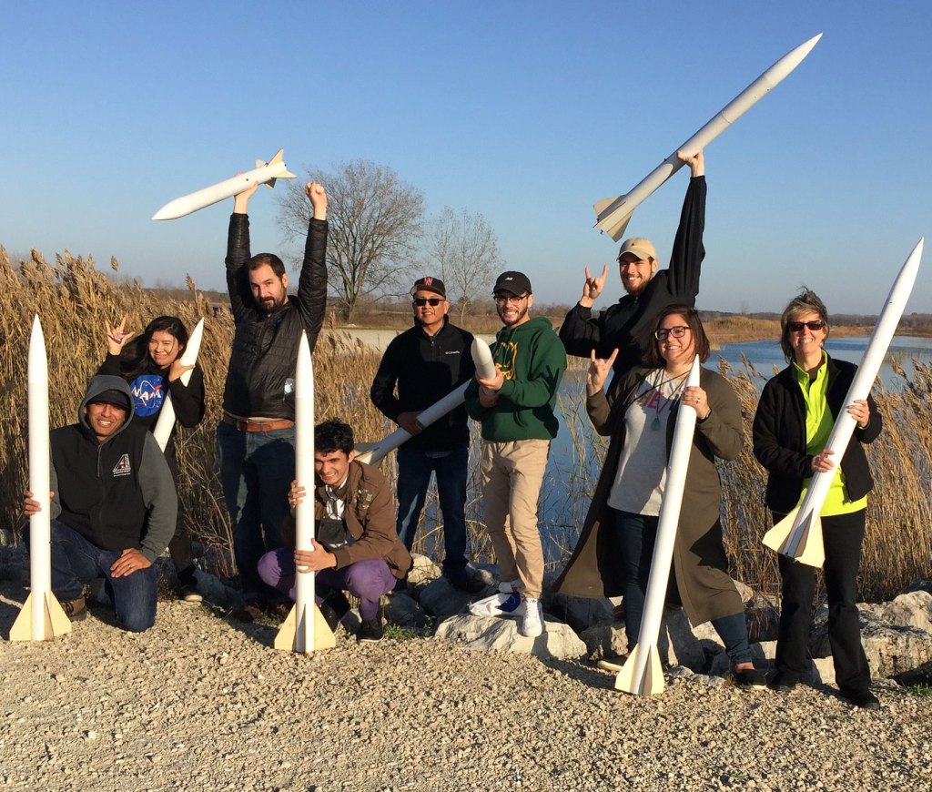 A group of First Nations Launch students holding rockets at a launch site