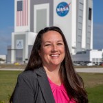 A photo of Kennedy Space Center's Elizabeth Kline with the Vehicle Assembly Building in the background.