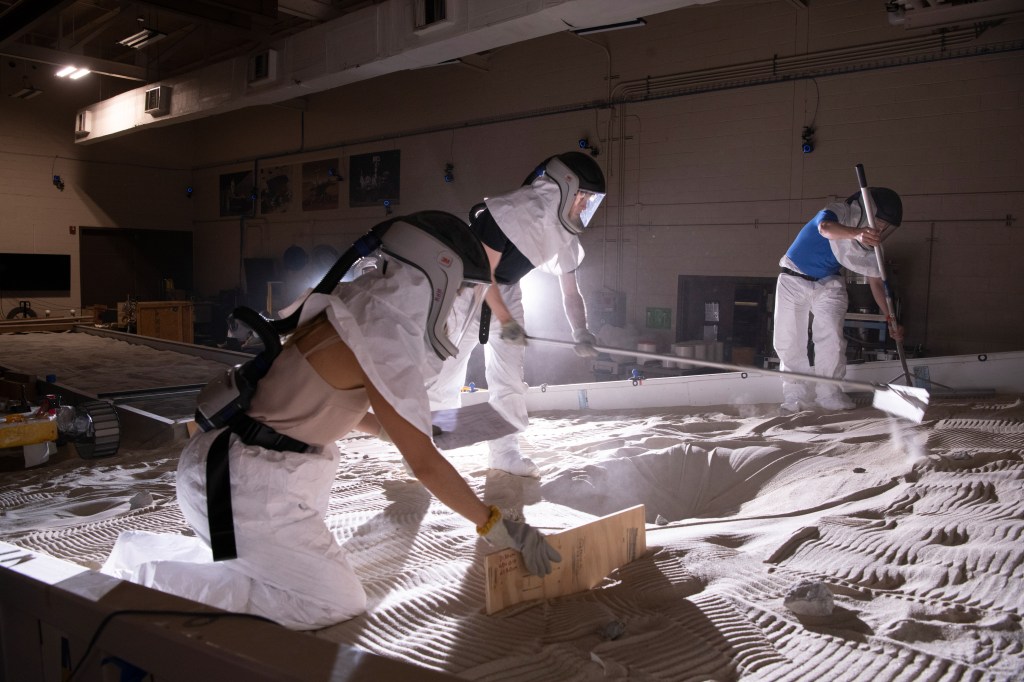 Researchers in protective equipment work with lunar simulant soil in the SLOPE lab at Glenn.