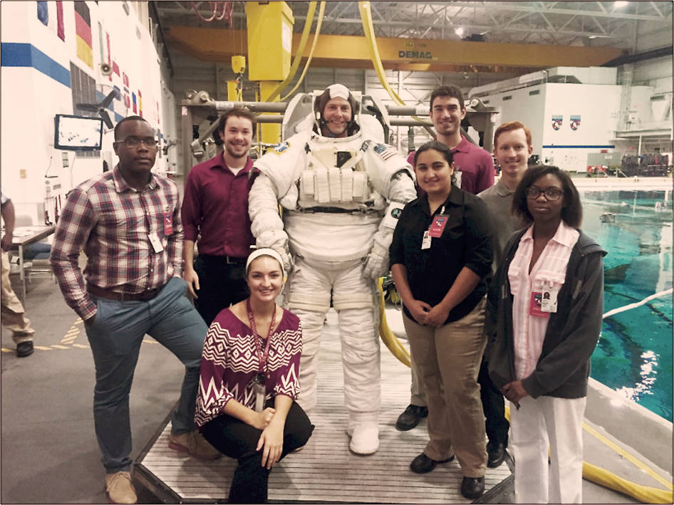 A group of eight people standing for a group photo. In the middle of the group is a person with an astronaut diving suit on.