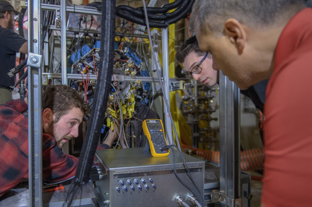 Three males gathered around test equipment.