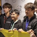 A group of 5 young men pose for a picture while holding a banner