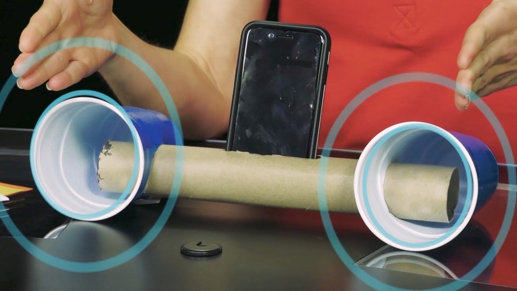 NASA employee running experiment with two plastic cups on either end of a paper towel empty roll with a cell phone in the middle.