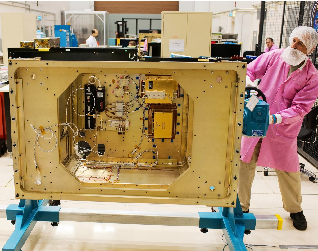 Fall 2010, software engineers work in the background of the West High Bay area of the Power Systems Facility as Glenn Research Center technician, Joe Kerka rotates the SCAN Testbed flight enclosure assembly using a specially manufactured mount. Flight components can be seen inside the flight enclosure. The SCAN Testbed will be launched on a Japanese H–IIB Transfer Vehicle and installed on the International Space Station (ISS) providing an on-orbit, adaptable software-defined radio (SDR) facility with corresponding ground and operational systems. This will permit mission operators to remotely change the functionality of radio communications through software once deployed to space, offering them flexibility to adapt to new science opportunities and recover from anomalies within the science payload or communication system. This effort is sponsored by NASA’s Space Communications and Navigation (SCaN) Program as part of the Communications, Navigation, and Networking reConfigurable Testbed (CoNNeCT) Project led by Glenn Research Center.