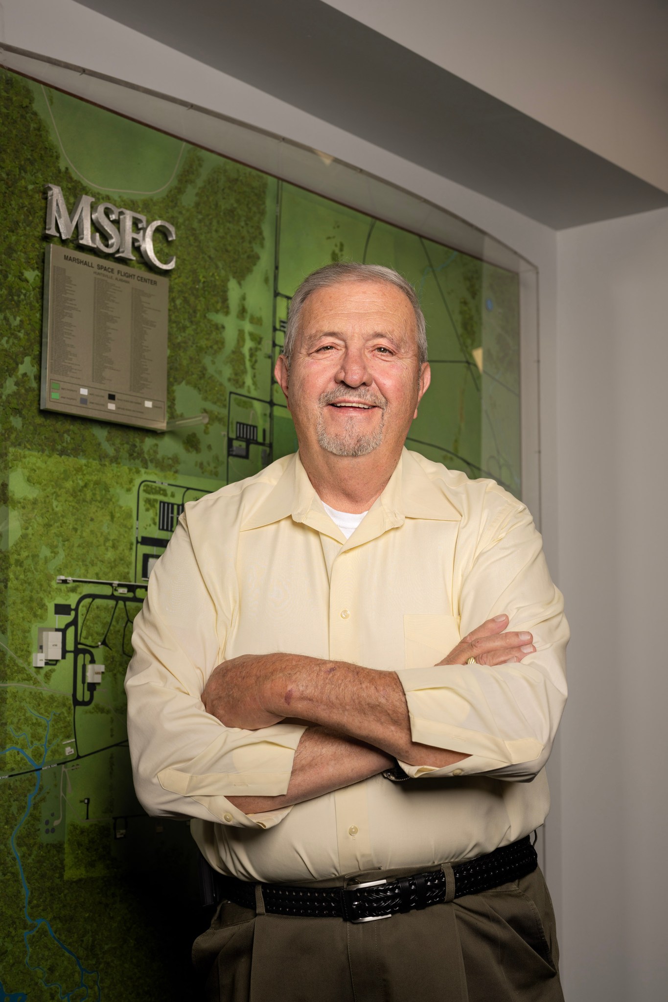 A white man stands with his arms crossed in front of a green wall.