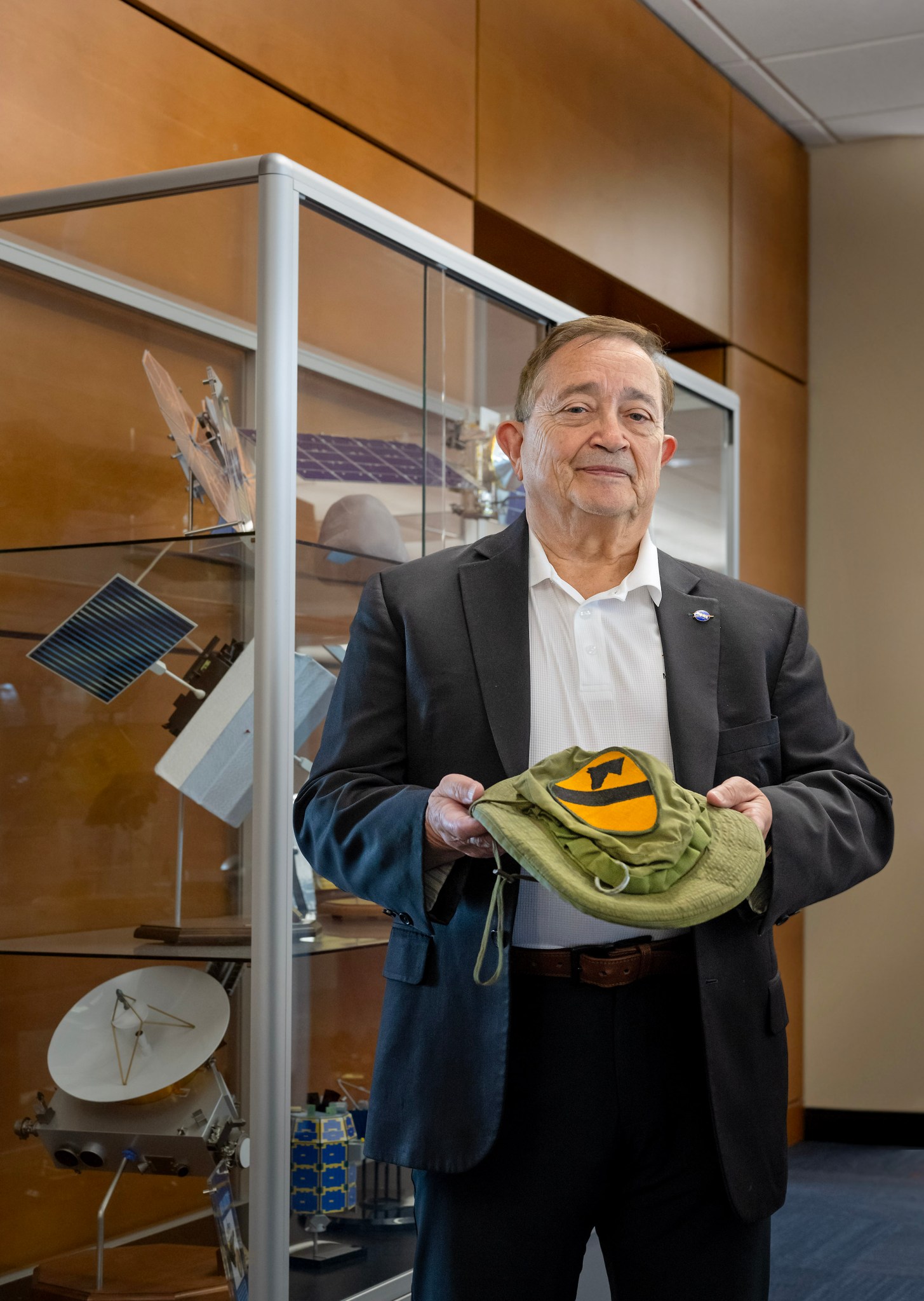 An older white man stands holding his green military hat