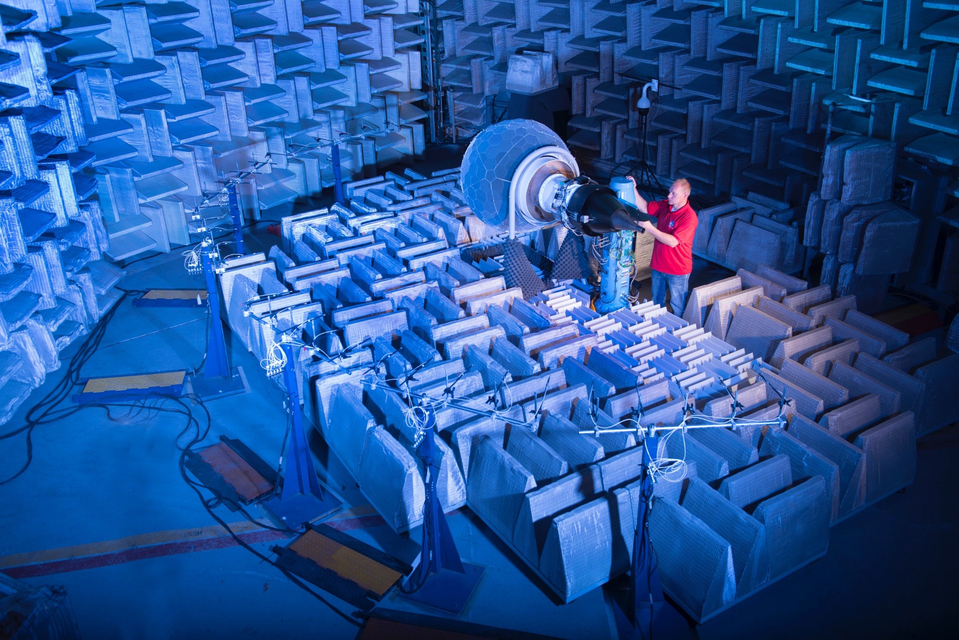 A person stands next to a small jet engine inside a soundproofed room.