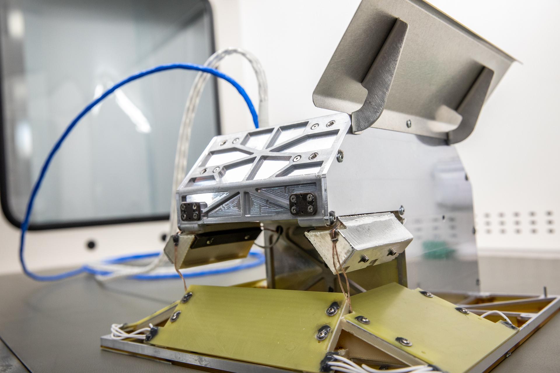 A electrodynamic dust shield device is centered in this photo with a blue wire in the background.