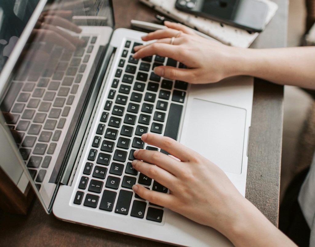 A woman's hands typing on a laptop at a desk.