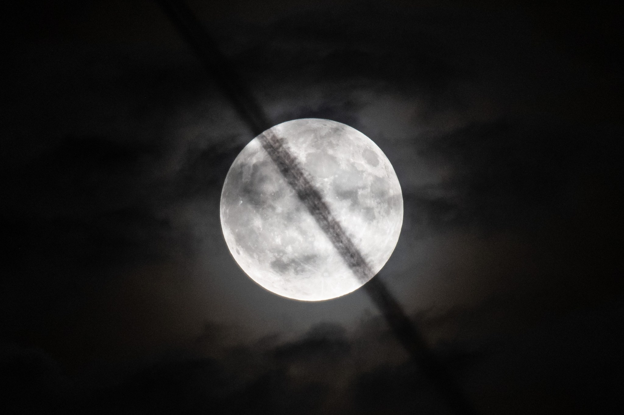 Up-close image of wispy aircraft contrails crossing the face of the Moon.