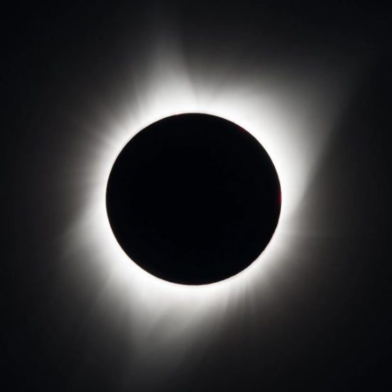 A total solar eclipse showing a darkened sun with a bright, glowing corona around its edges.